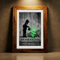 A monochromatic Banksy-style street art print of a hooded child watering a glowing neon green plant growing from a cracked wall with stenciled text reading HOPE GROWS IN THE CRACKS, created by Artazyn.
