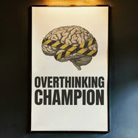 Framed poster with brain illustration and 'Overthinking Champion' text on a rustic wall.