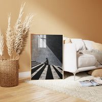 High-contrast black and white illustration of a figure sitting on striped steps with dramatic geometric shadows.